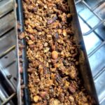Metal, half-cylindrical-shaped solar oven tray holds golden brown toasted granola.