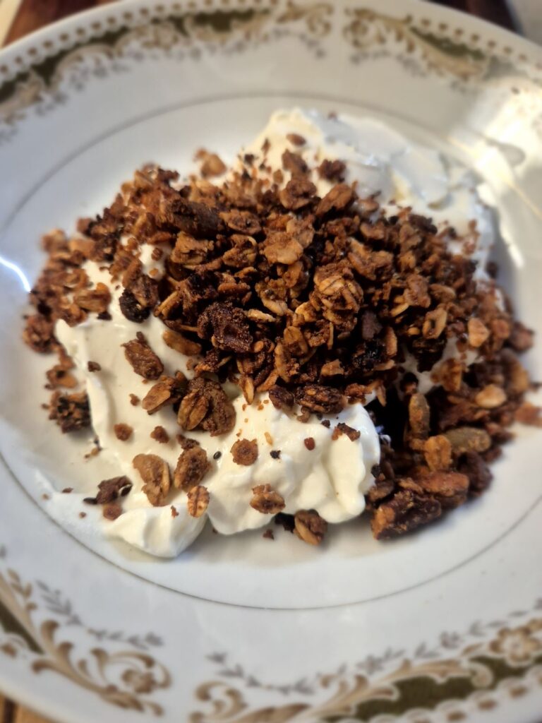 Crunchy sourdough granola clusters served over Greek yogurt in a shallow china bowl