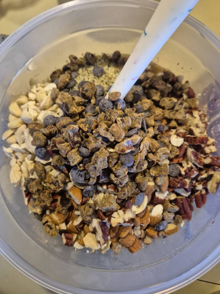 Clear plastic bowl containing now with chopped dried dates and carob chips on top of the rest of the dry ingredients.